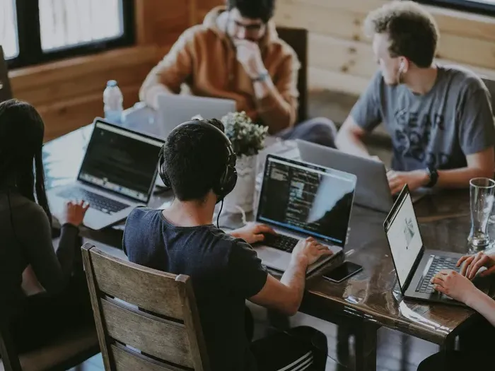 Startup team collaborating on laptops around a wooden table in a modern workspace focused on a software project